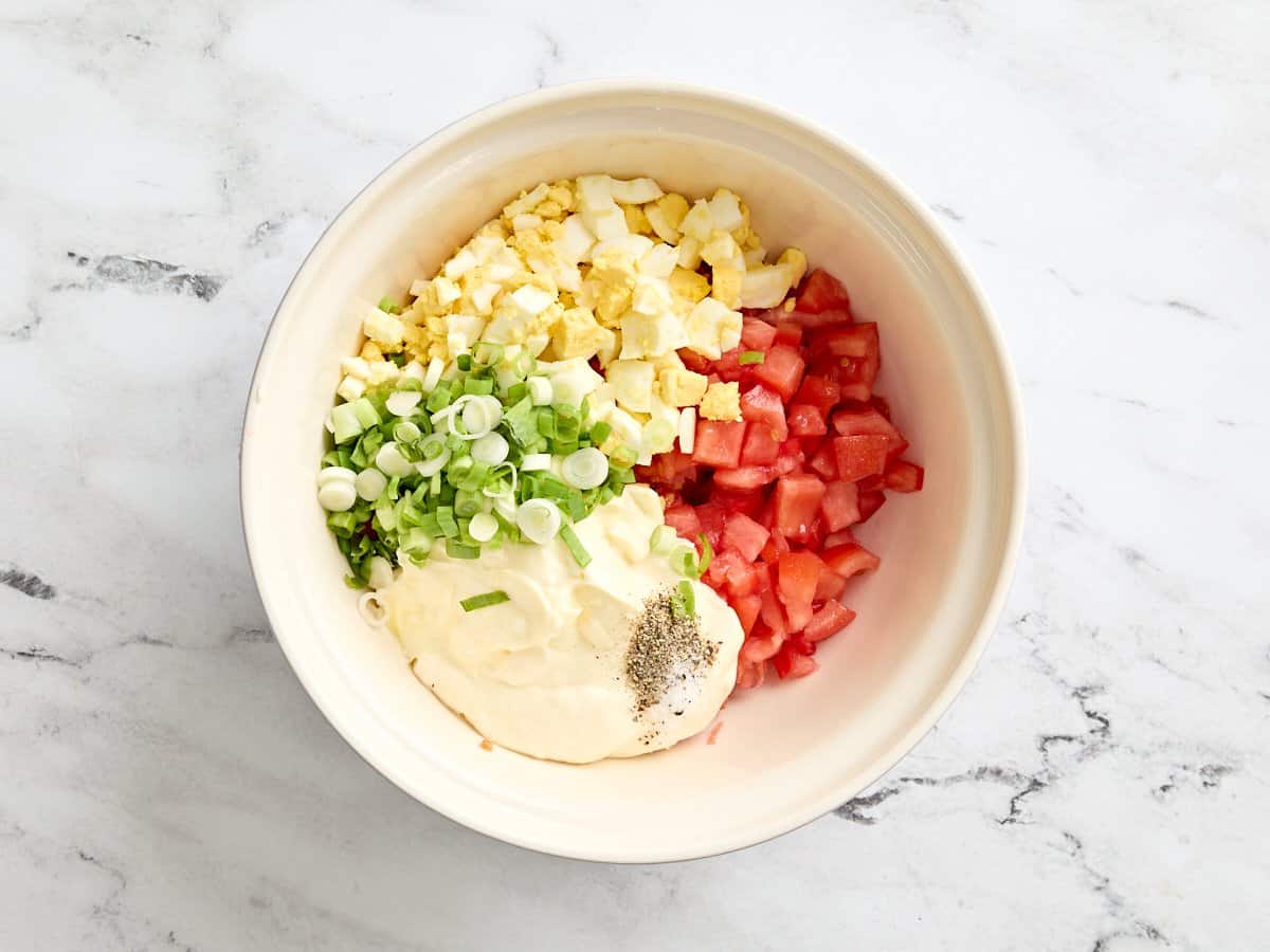 Diced hard boiled eggs, sliced green onions, diced tomatoes, mayonnaise, and seasonings in a mixing bowl.