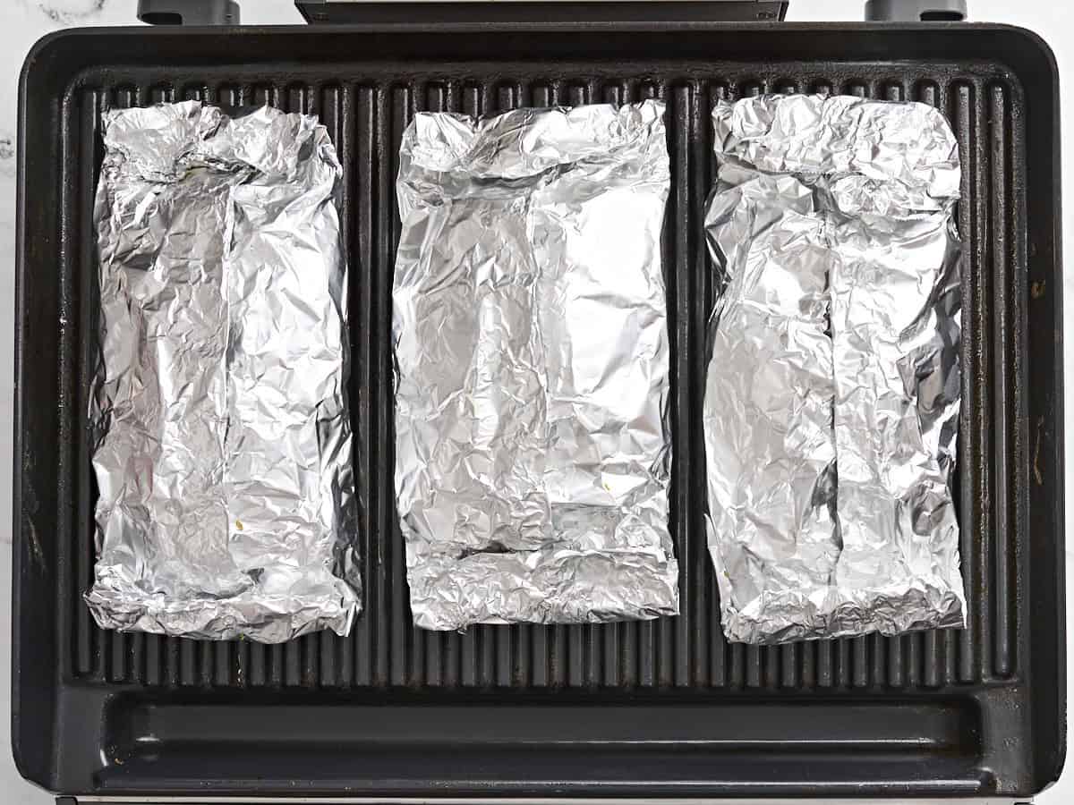 Foil packets cooking on a grill.