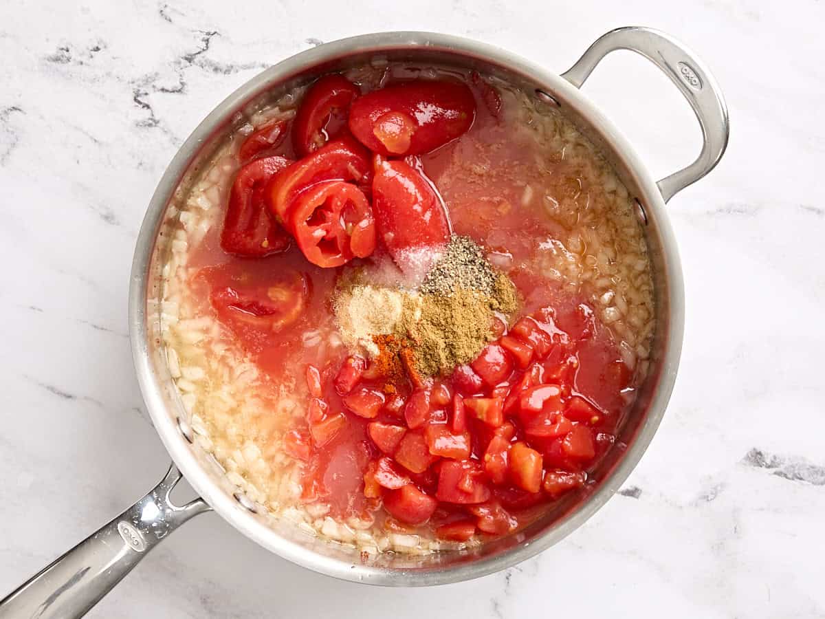 Canned tomatoes and seasoning added to sauteed onions in a skillet.