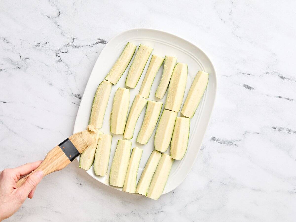 A brush coating zucchini spears with mayo and dijon mix.