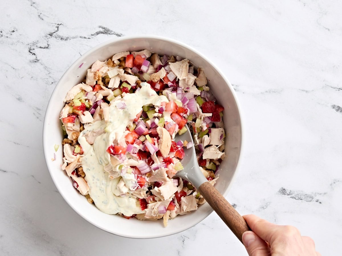 Strawberry chicken salad ingredients being combined in a bowl with a wooden spoon.