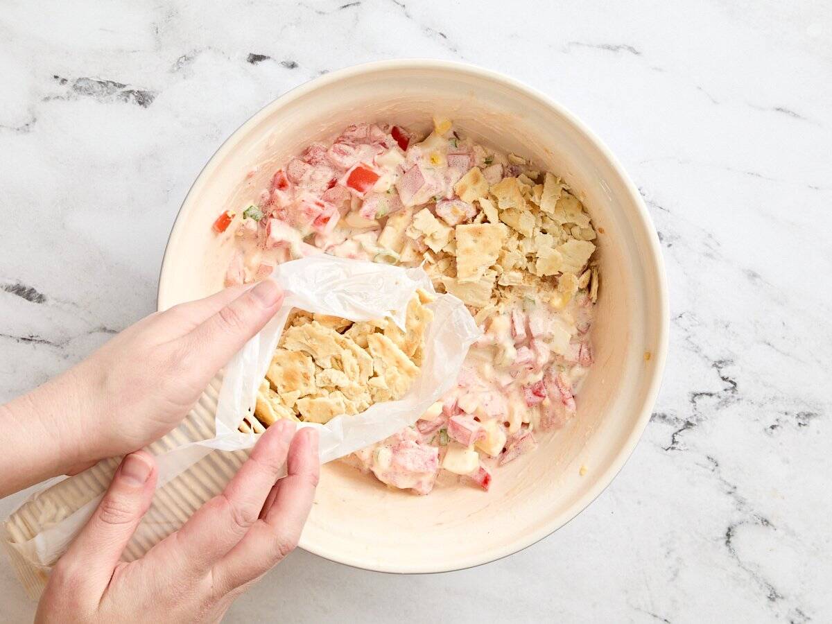 Crushed saltine crackers being added to a bowl of cracker salad.