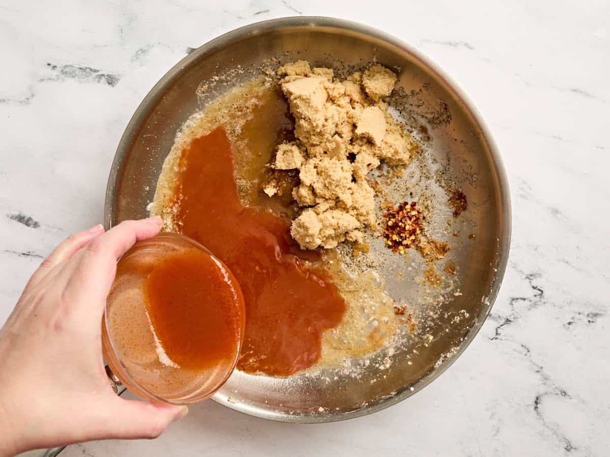 Buffalo sauce being added to a skillet with brown sugar.