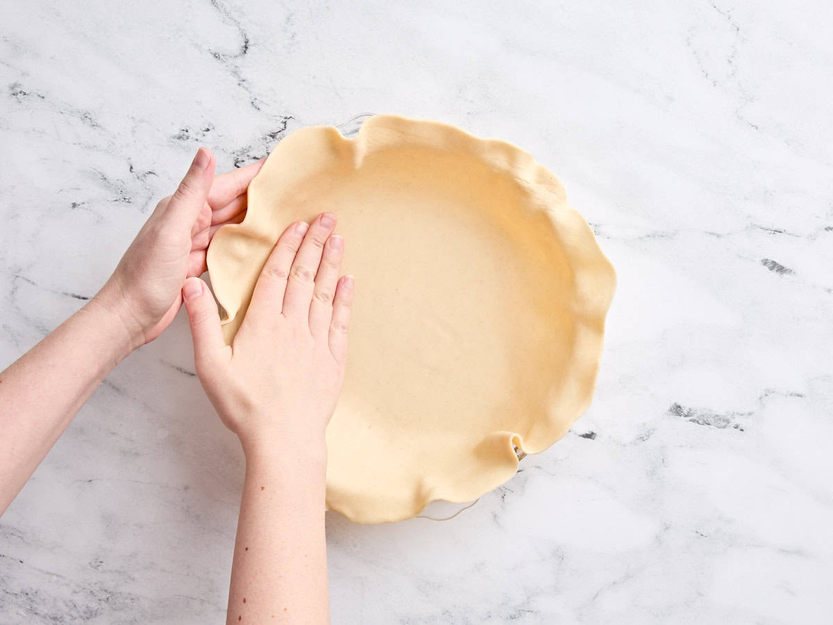 Hands pressing a pie crust into a pie dish.