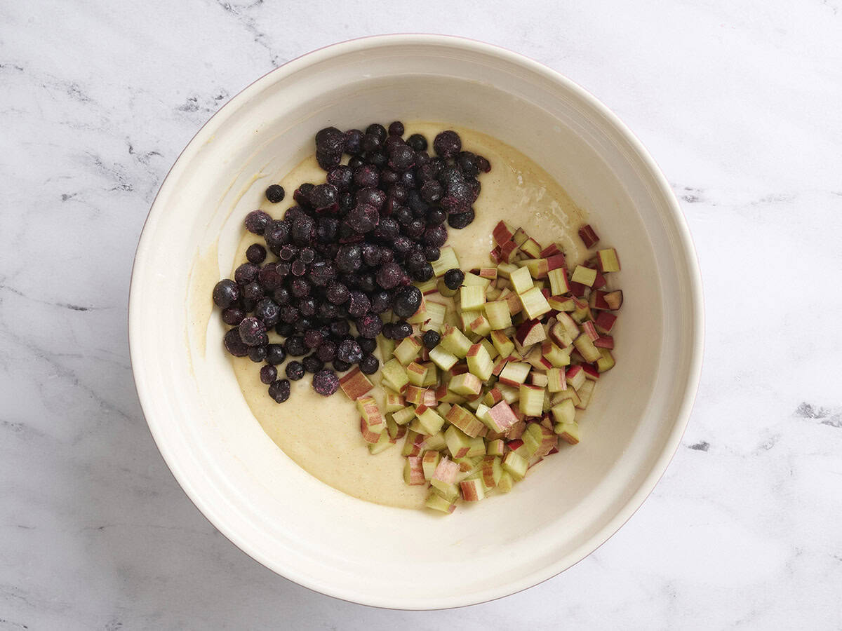 Blueberries and rhubarb added to a bowl of muffin batter.