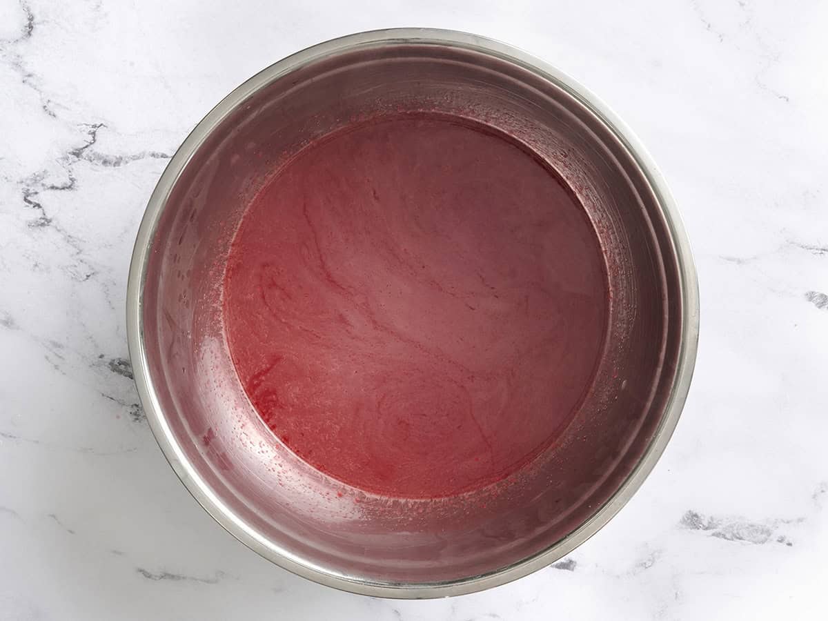 Hot water and strawberry jello mix in a bowl.