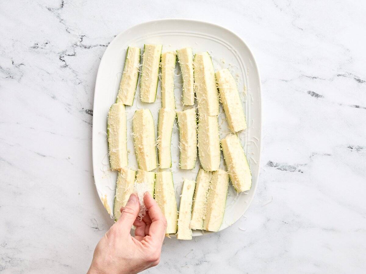 A hand sprinkling breadcrumbs and parmesan on zucchini spears.