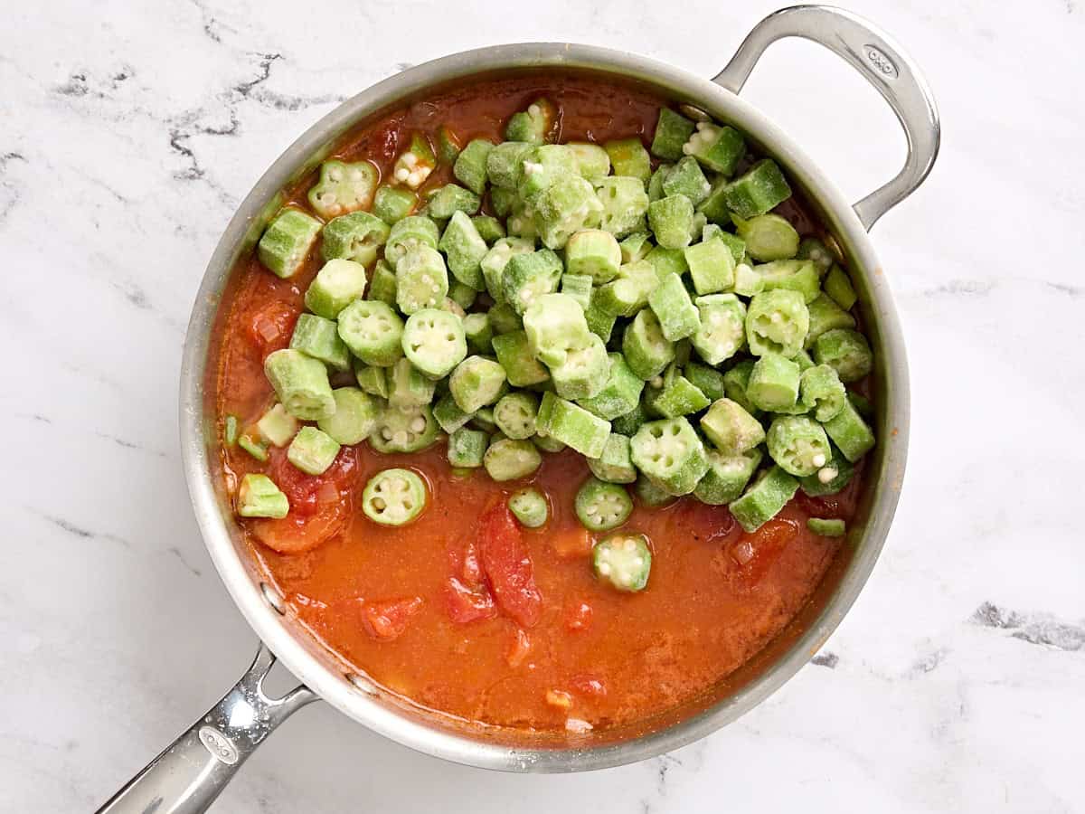Frozen okra added to stewed tomatoes in a skillet.