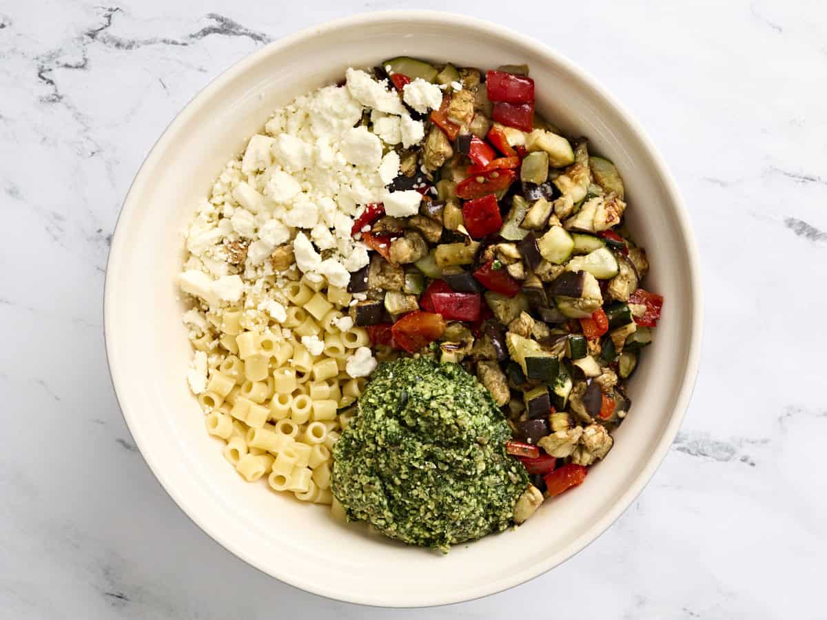 Feta cheese, roasted summer vegetables, cooked ditalini pasta, and pesto in a bowl.