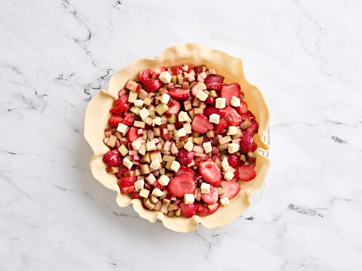 Rhubarb and strawberry filling added to a pie crust in a pie dish, topped with diced butter.
