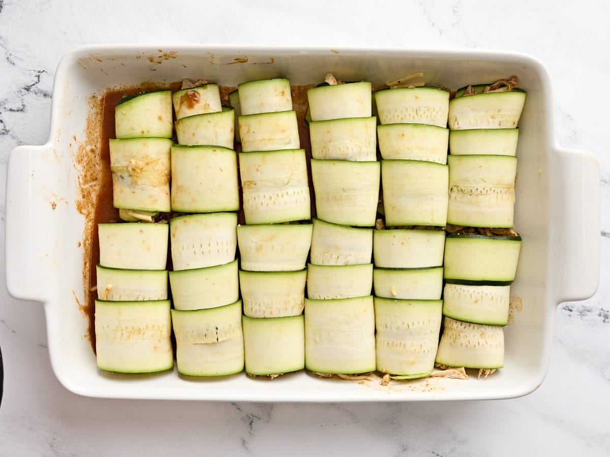 Rolled zucchini enchiladas in a baking dish.