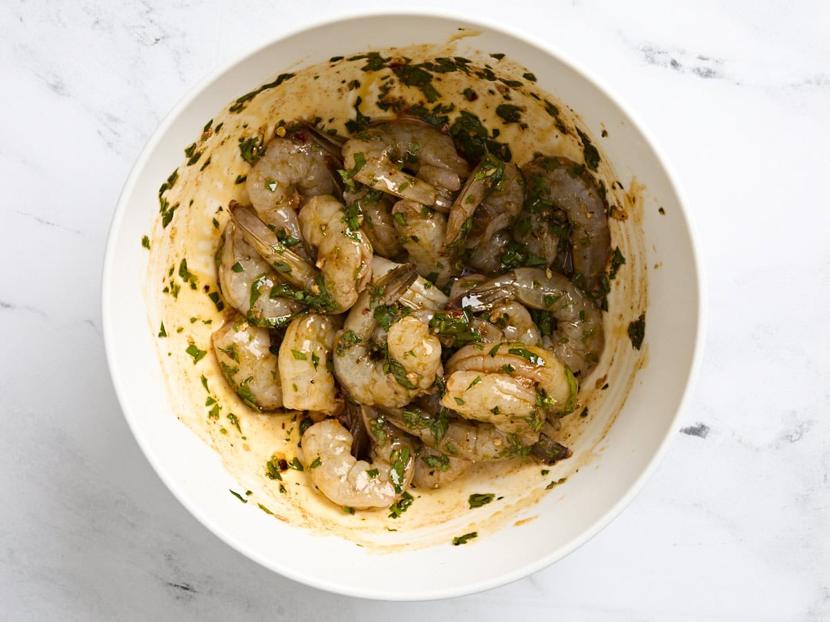 Raw shrimp mixed in a garlic and herb marinade in a bowl.