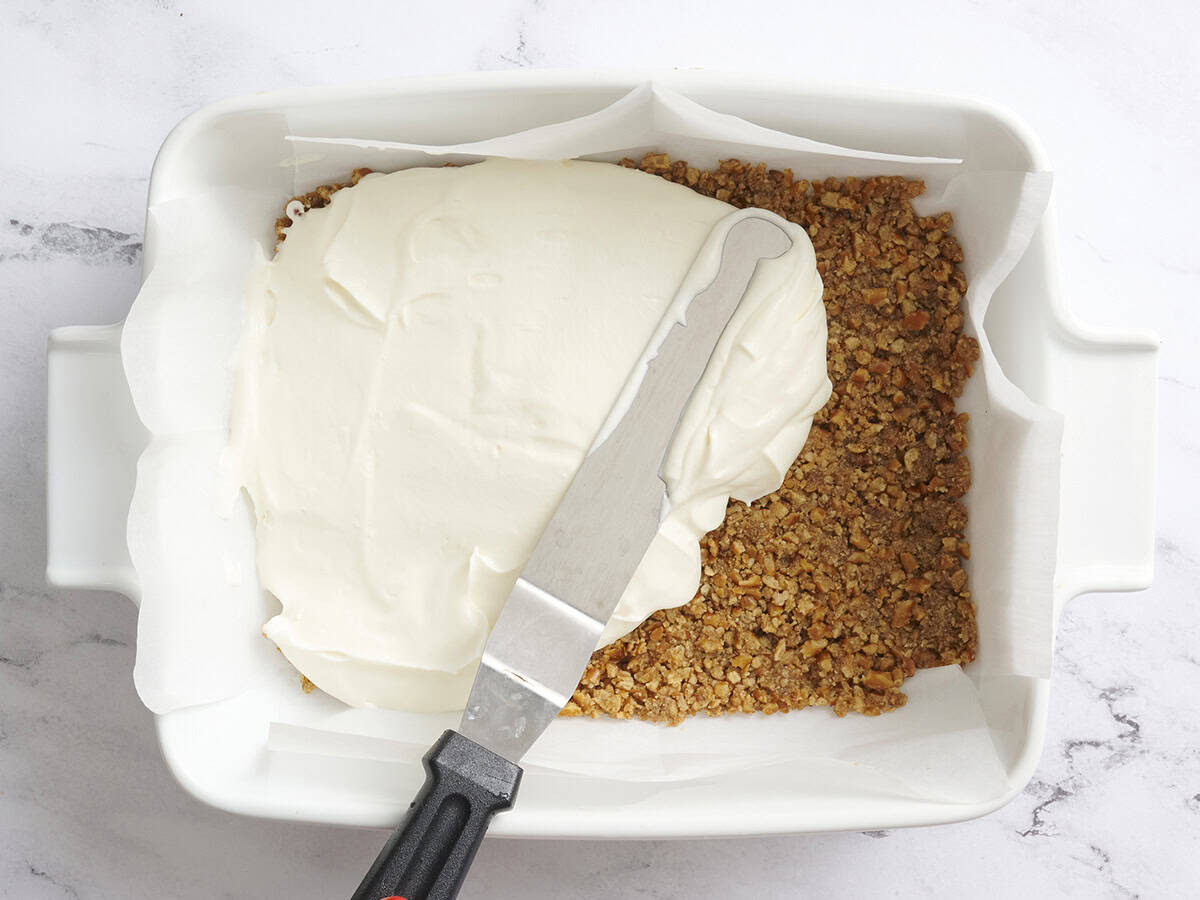 The cream cheese layer being spread on the pretzel layer for strawberry pretzel salad.