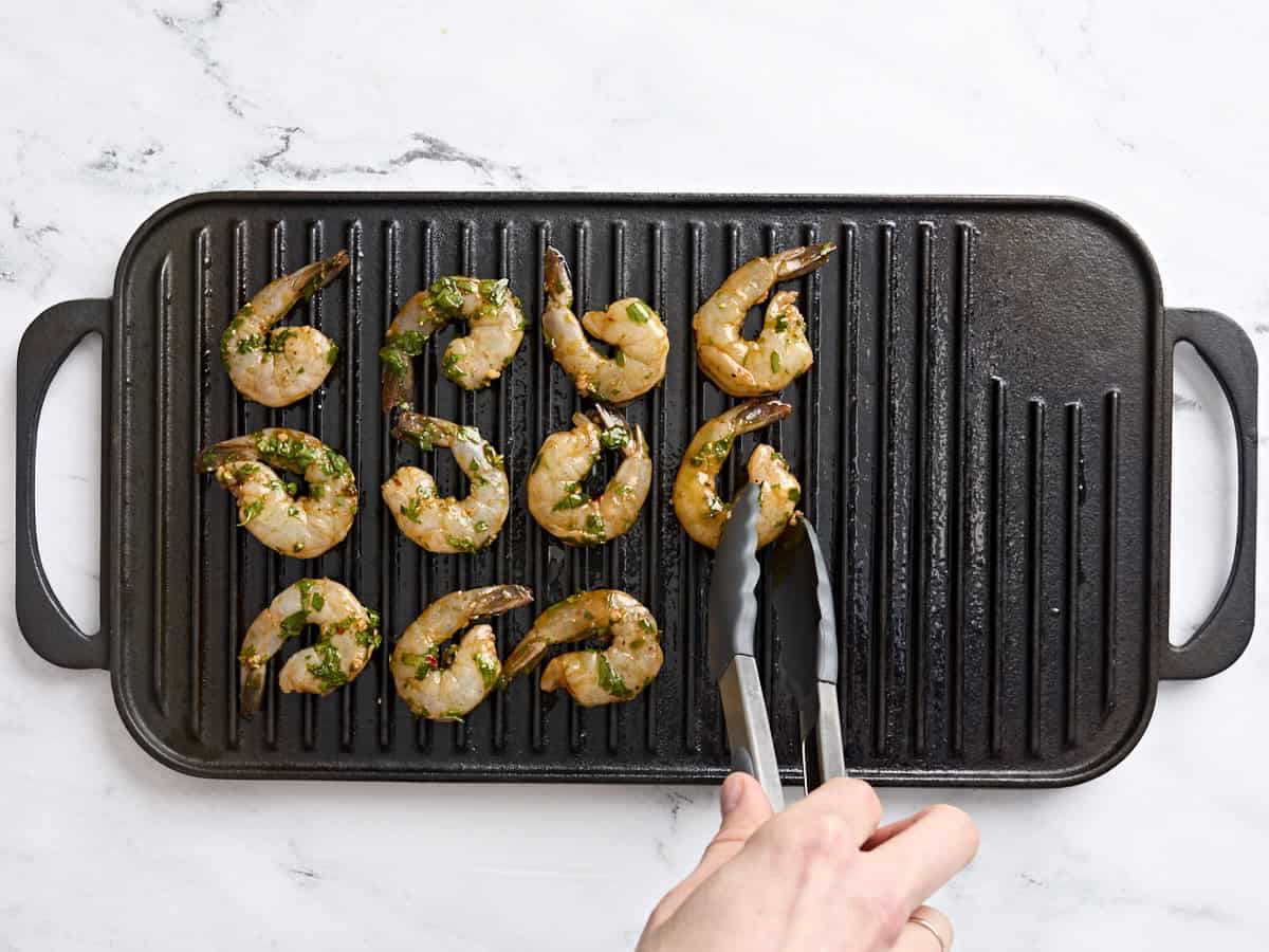 Marinated shrimp being added to a grill.