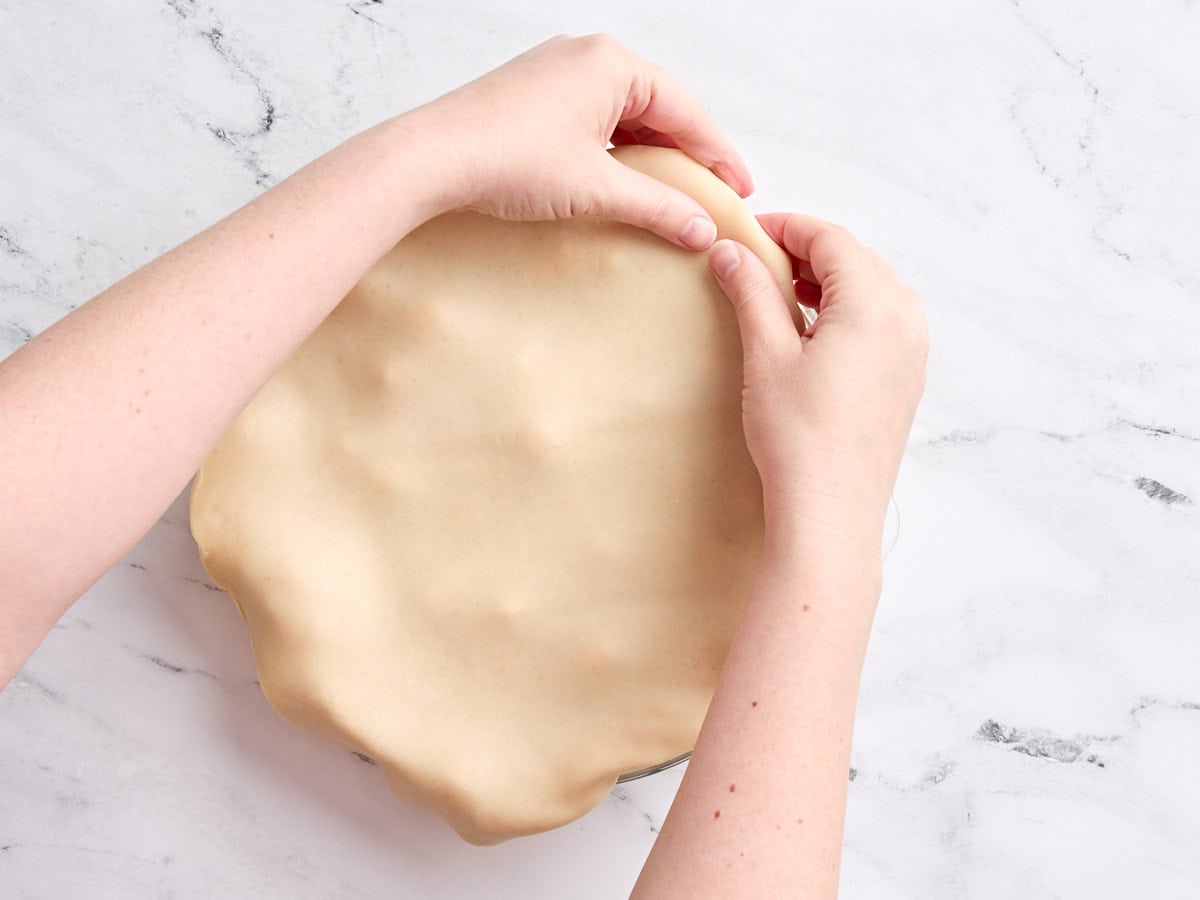 Hands crimping the edges of a pie crust in a pie dish.
