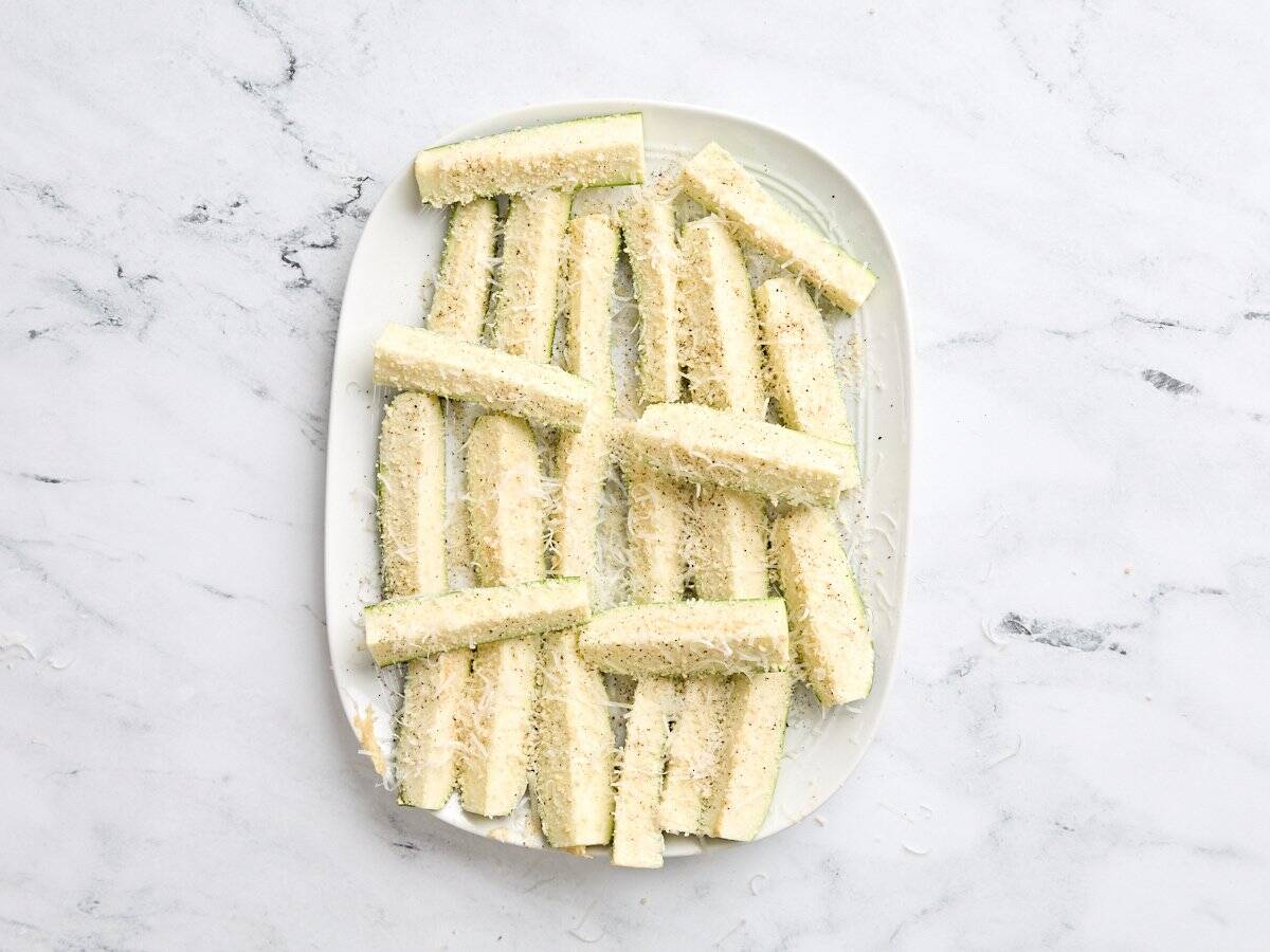 Salt and pepper added to breaded zucchini spears.