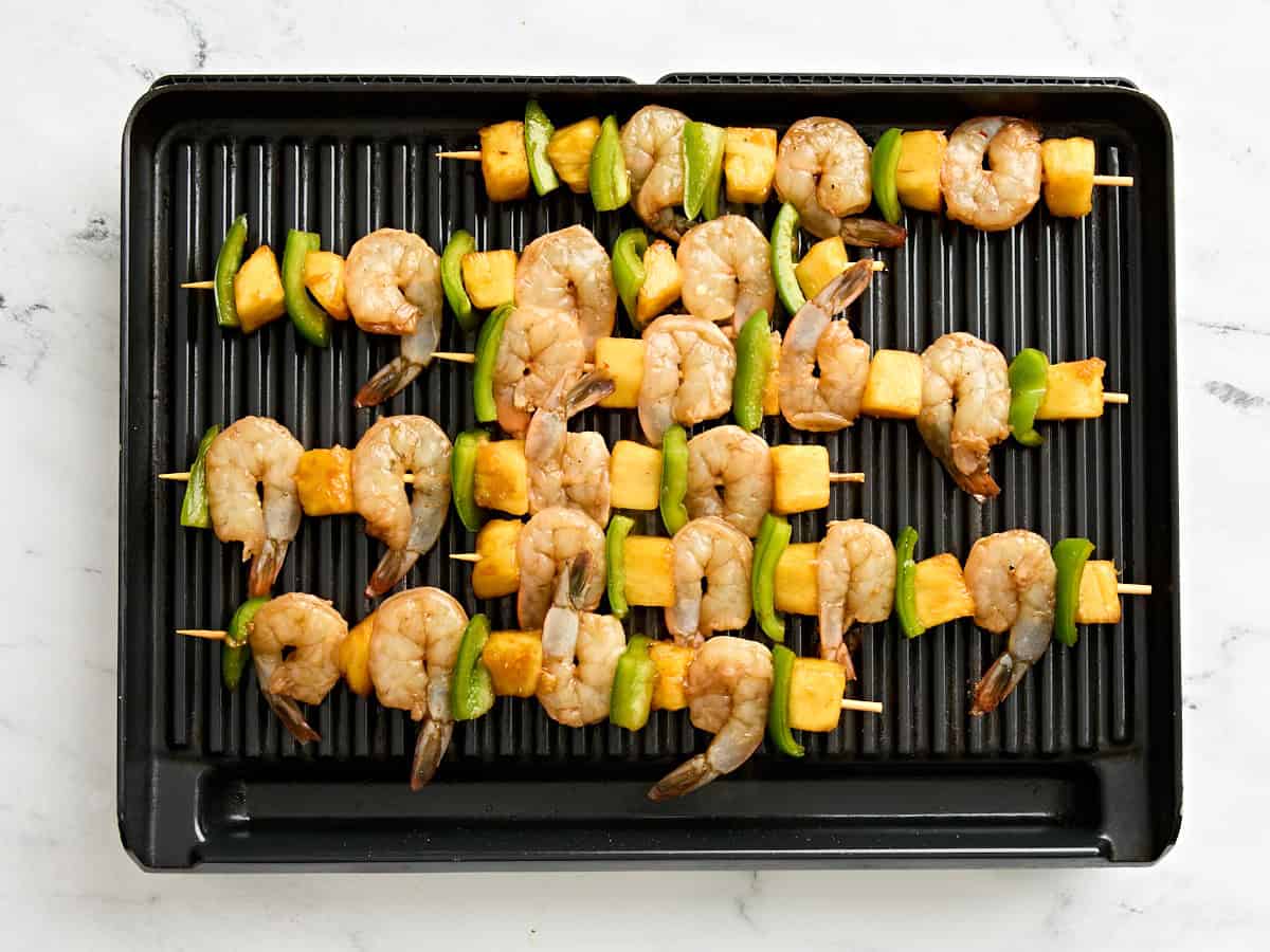 Shrimp and pineapple skewers on a grill.