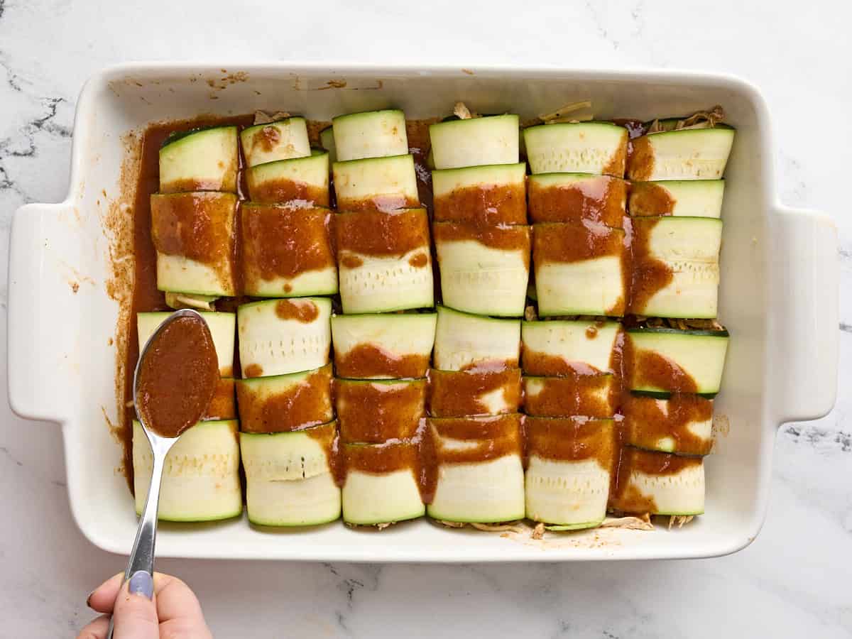 Zucchini enchiladas topped with enchilada sauce in a baking dish.