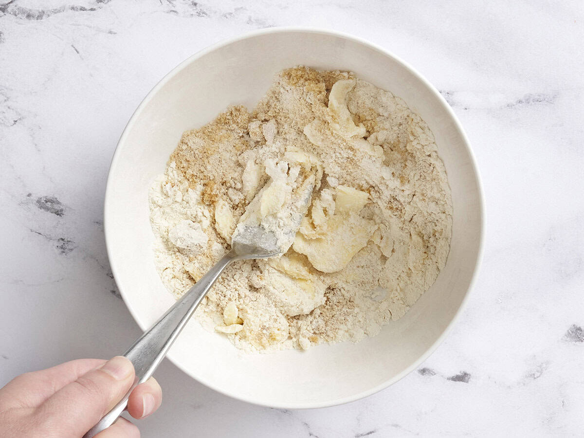 A fork mixing the ingredients for a streusel topping in a mixing bowl.
