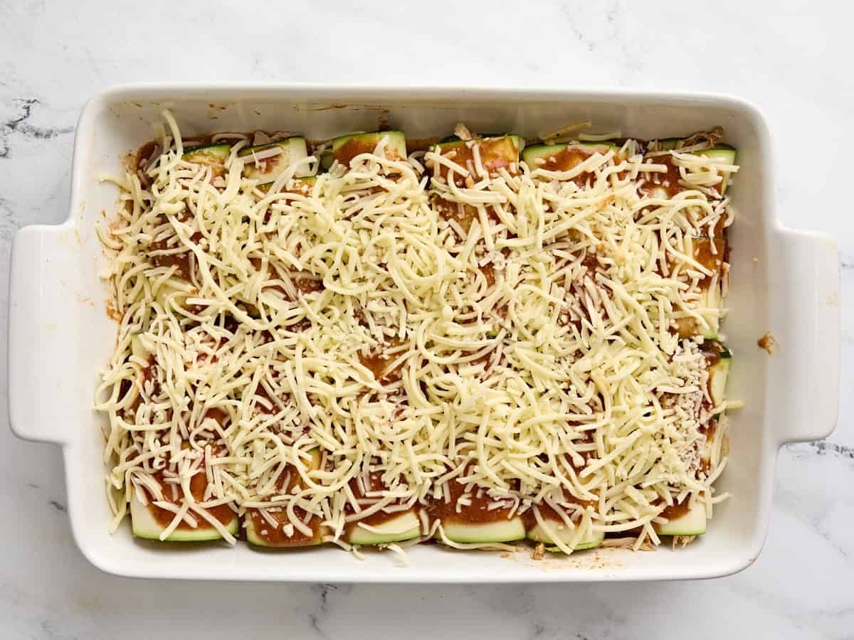 Homemade zucchini enchiladas topped with cheese and enchilada sauce in a baking dish.