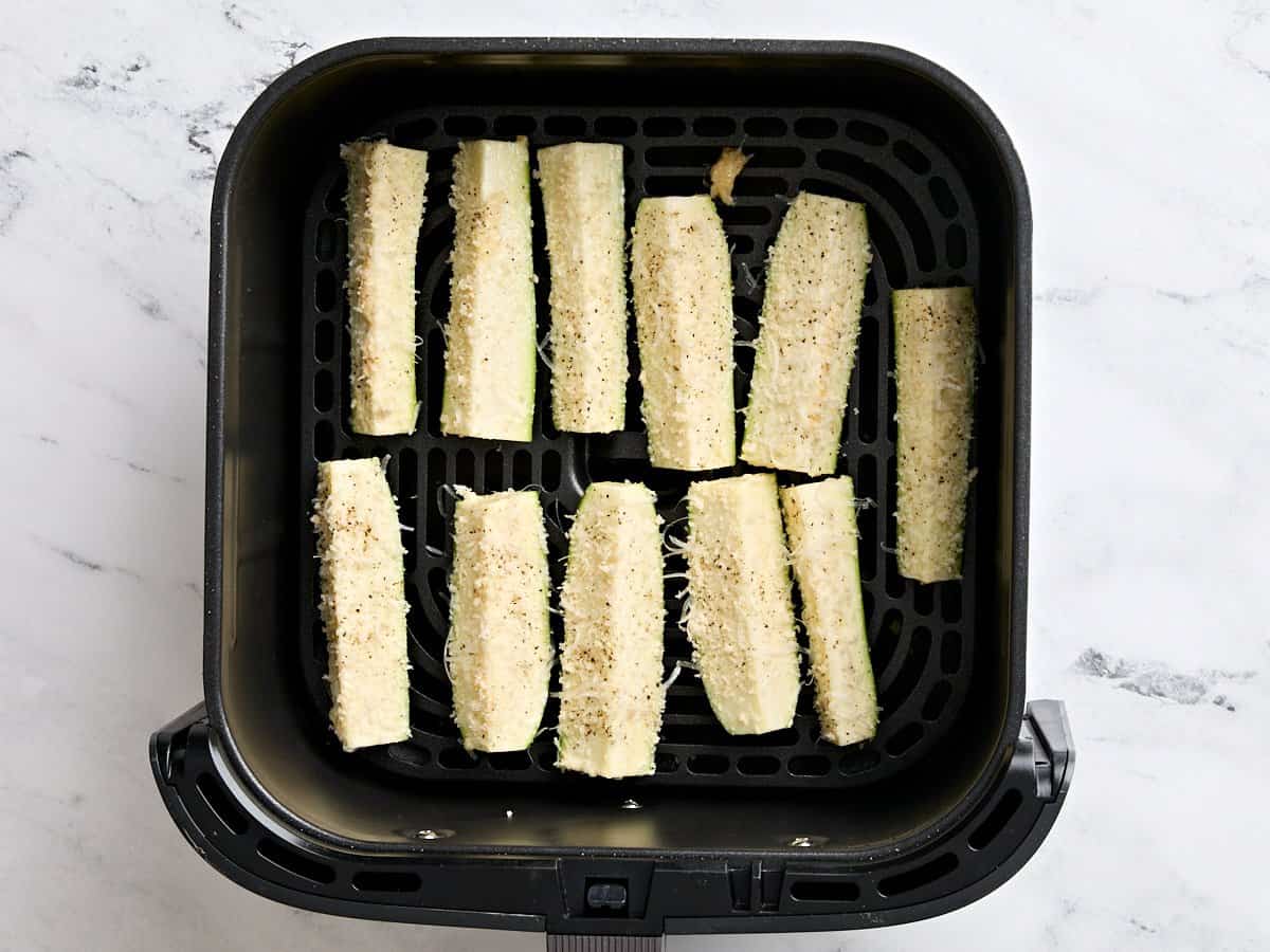 Breaded zucchini spears in an air fryer basket.