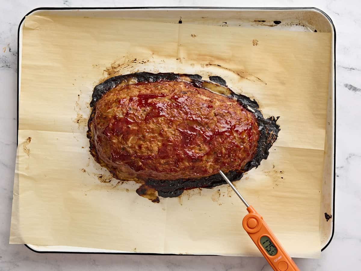 A meat thermometer checking the internal temperature of a freshly baked turkey meatloaf on a parchment lined baking sheet.