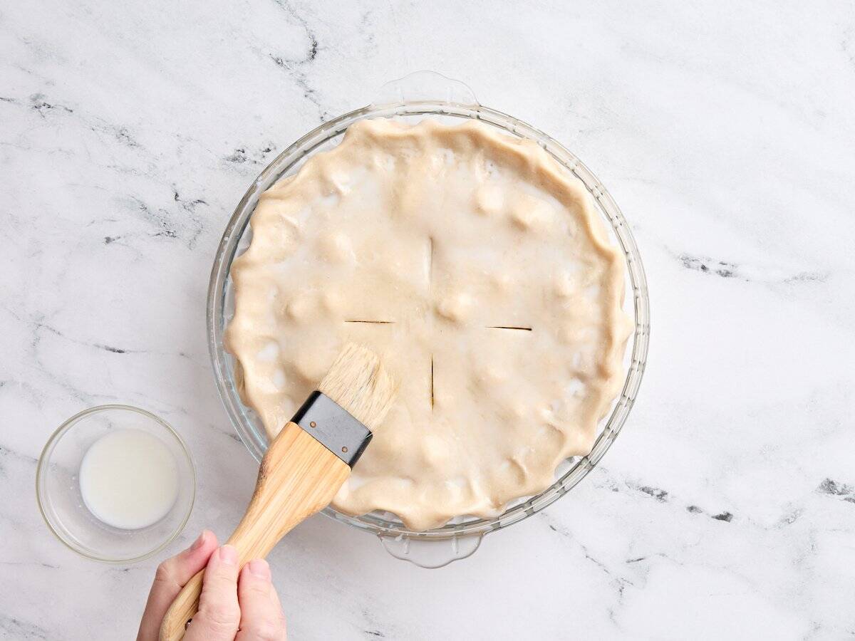An unbaked rhubarb and strawberry pie being brushed with milk.