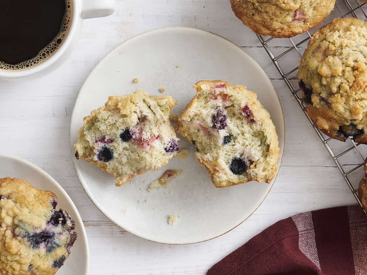 A homemade rhubarb blueberry muffin sliced in half on a plate.