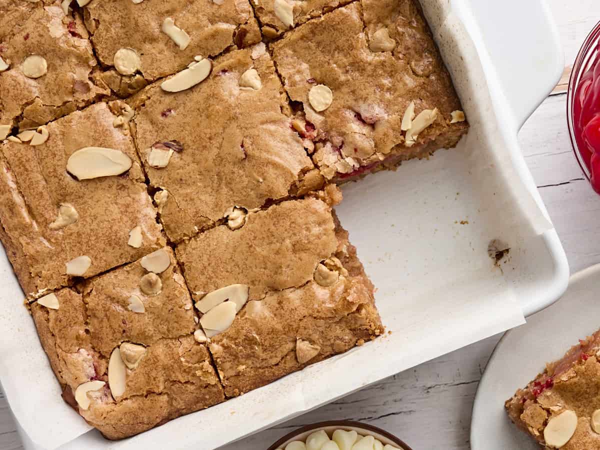 Overhead view of a baking dish of cherry blondies with one missing.