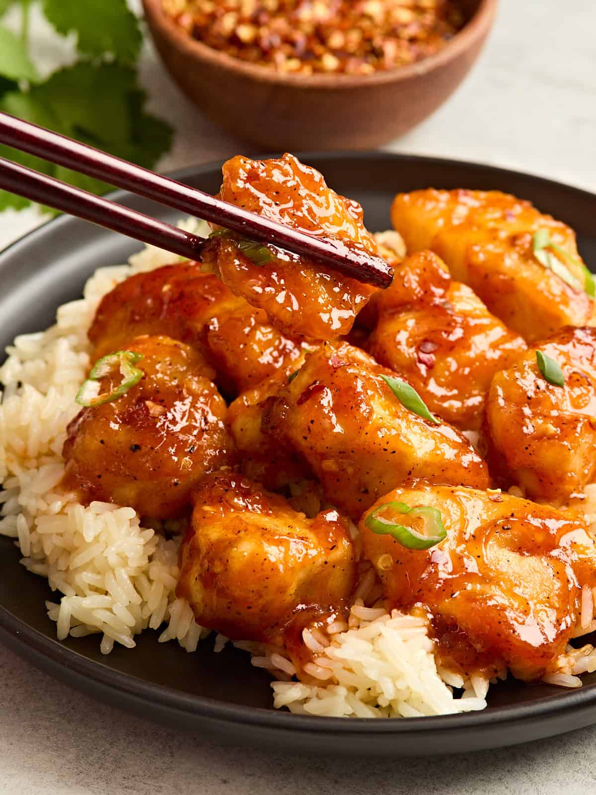 Side view of firecracker chicken on a bed of rice with one piece being taken by chop sticks.