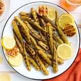 Overhead view of grilled okra on a plate with lemon slices.