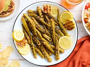Overhead view of grilled okra on a plate with lemon slices.