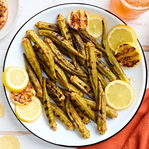 Overhead view of grilled okra on a plate with lemon slices.