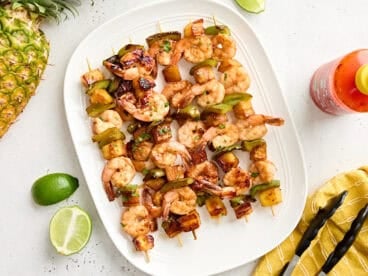 Overhead view of a platter of grilled shrimp and pineapple skewers.