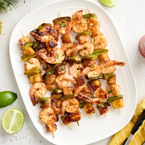 Overhead view of a platter of grilled shrimp and pineapple skewers.