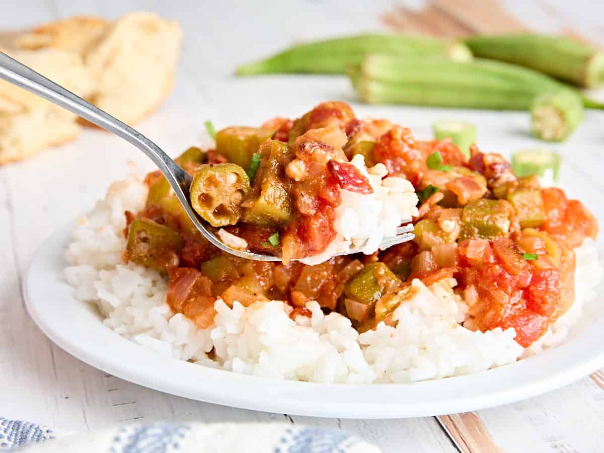 Side view of cooked tomatoes and okra on a bed of rice, with a fork taking some.