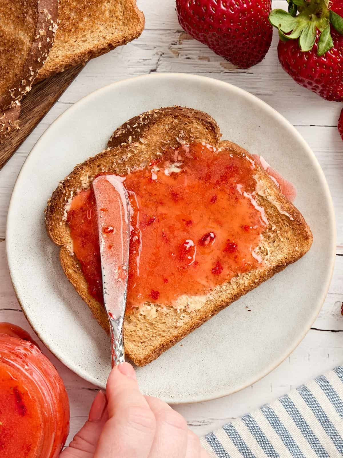 Overhead view of strawberry freezer jam being spread on toast.