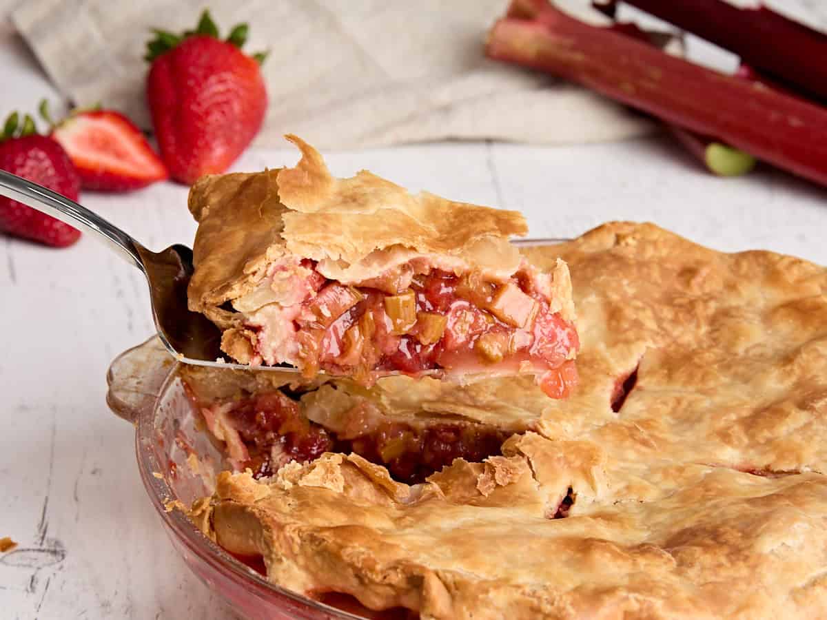 Side view of a slice of strawberry rhubarb pie being taken from a pie dish.