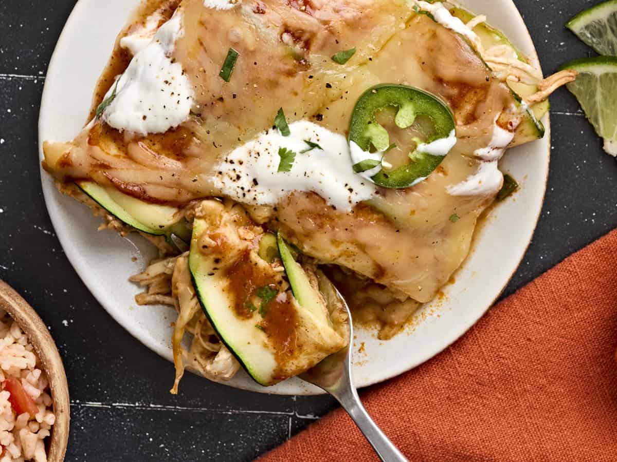 Overhead view of two zucchini enchiladas on a plate with a fork taking some.