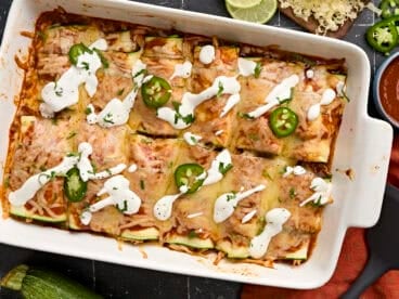 Overhead view of zucchini enchiladas topped with sour cream and sliced jalapenos.