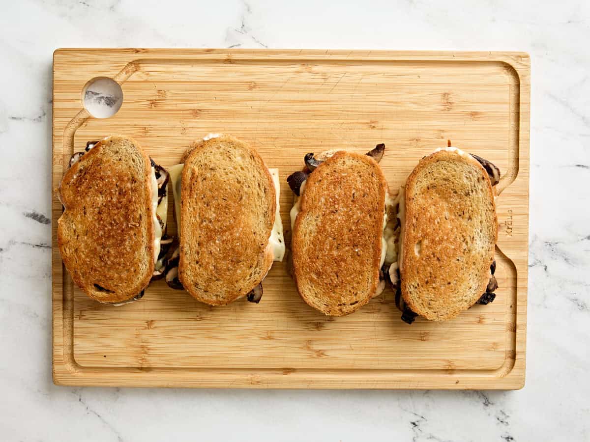 Overhead view of four mushroom patty melts on a wooden cutting board.