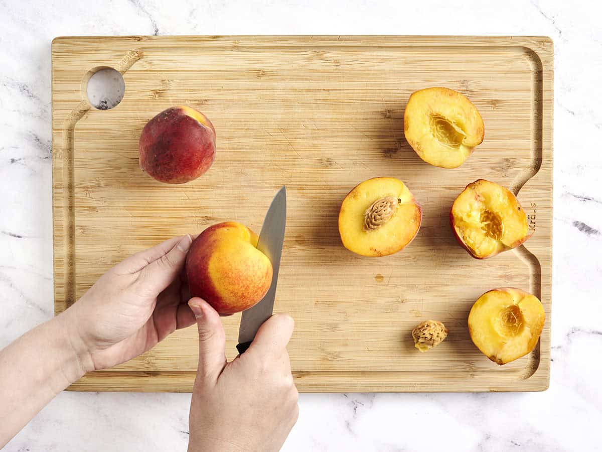 A hand using a knife to cut and pit peaches.