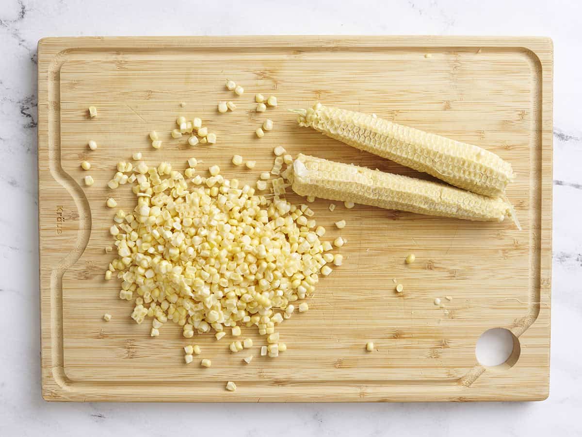 Two corn cobs with the kernels removed on a wooden cutting board.