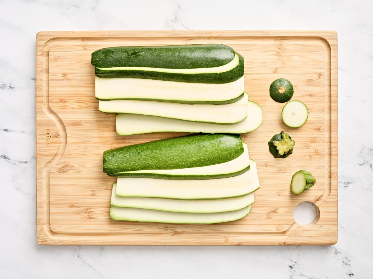 Fresh zucchini cut into slices with the top and ends removed on a wooden cutting board.