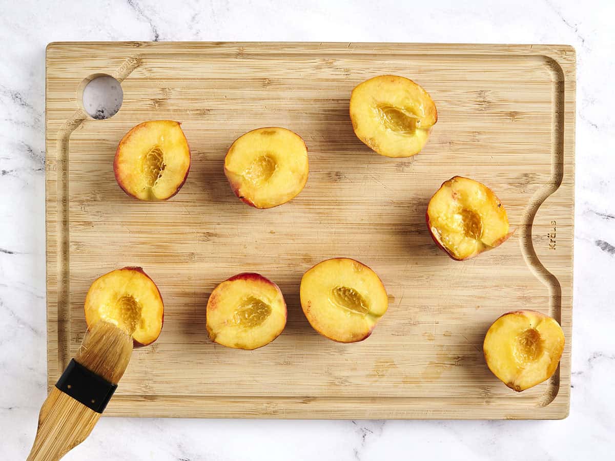 A brush brushing peach halves with oil.