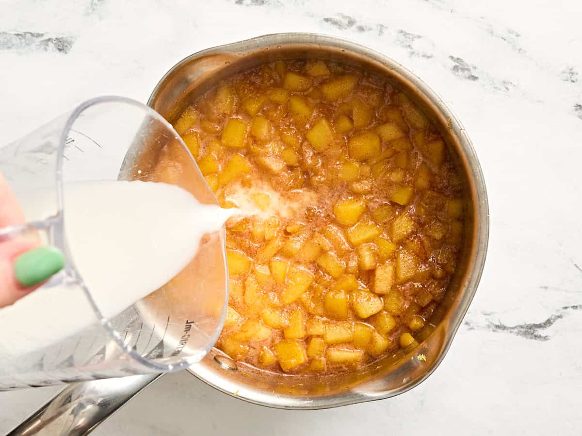 Cornstarch slurry being poured into peach sauce in a sauce pot.