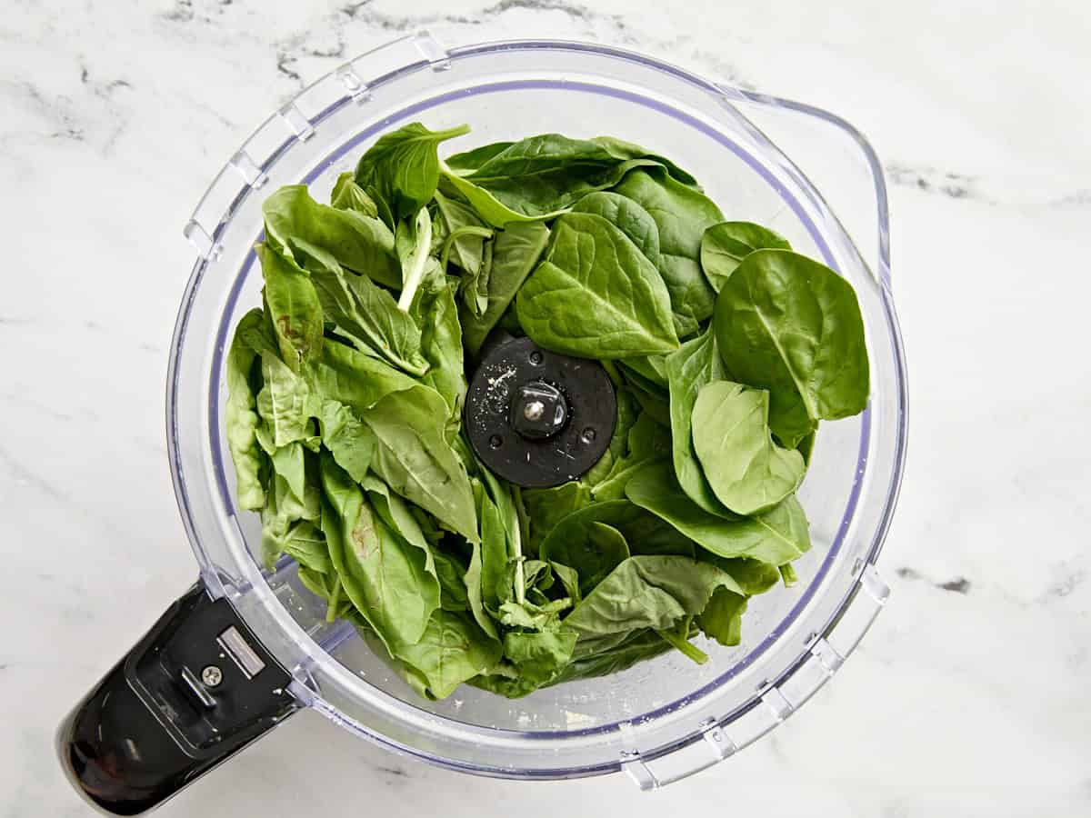 Spinach and basil added to a food processor.