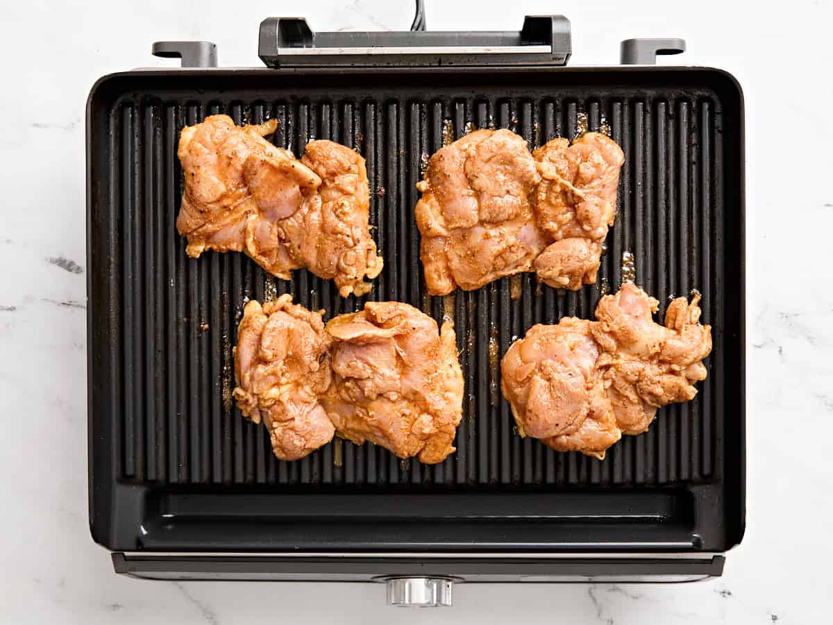 Marinated chicken thighs on a grill.