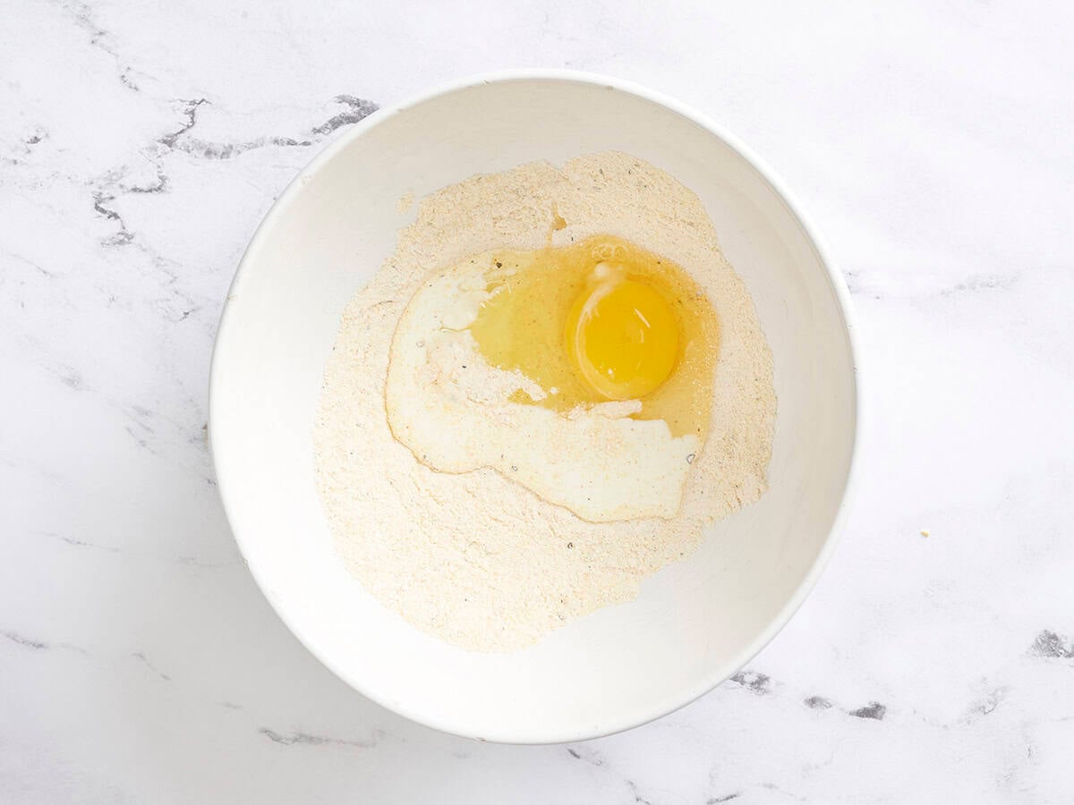 An egg and heavy cream added to a mixing bowl with dry ingredients for sweet corn fritters.
