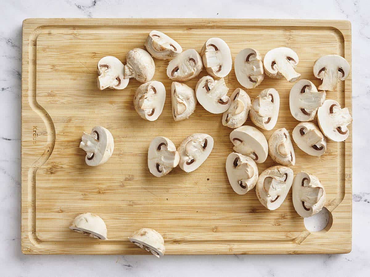 White mushrooms sliced in half on a wooden cutting board.